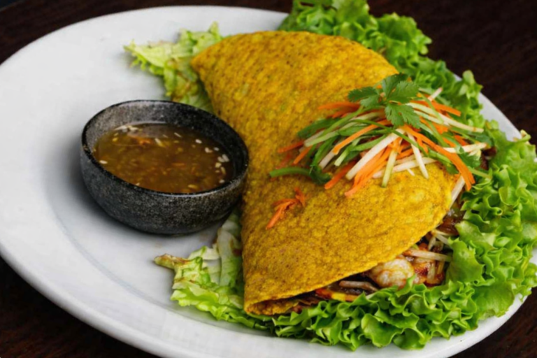 A golden Vietnamese crepe (bánh xèo) filled with shrimp, caramelized pork, and crisp vegetables, served with fresh lettuce leaves and a bowl of nước chấm at 533 Viet Fusion in Palm Springs.