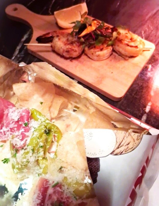 Nachos Españoles topped with cured meat and peppers alongside Gambas Pintxo shrimp skewers on a dark table