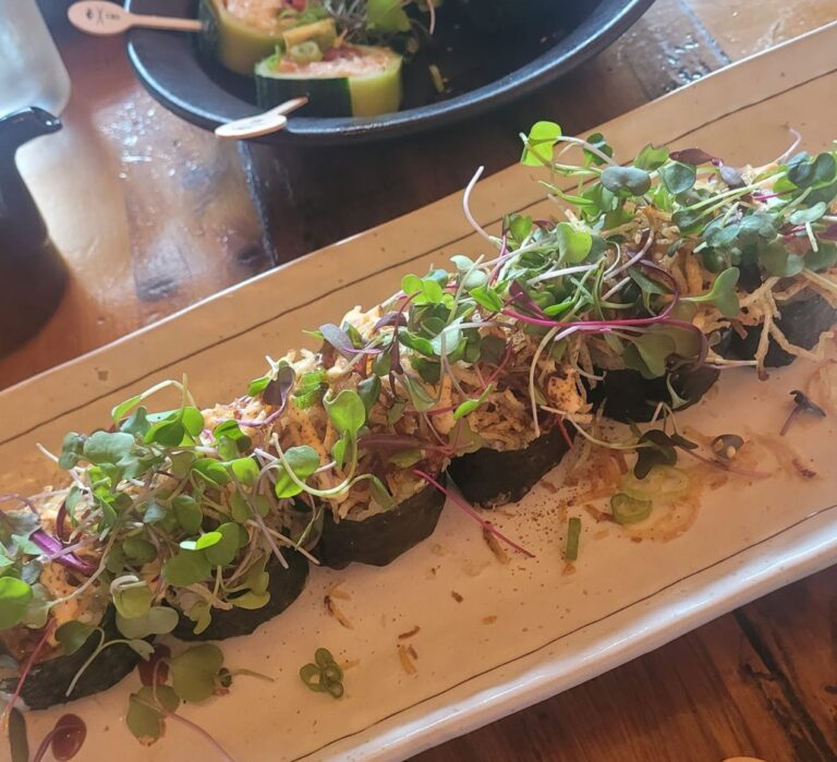 The Sandfish Roll at Sandfish Sushi & Whiskey in Palm Springs, topped with microgreens, potato threads, and black roe on a dark plate.