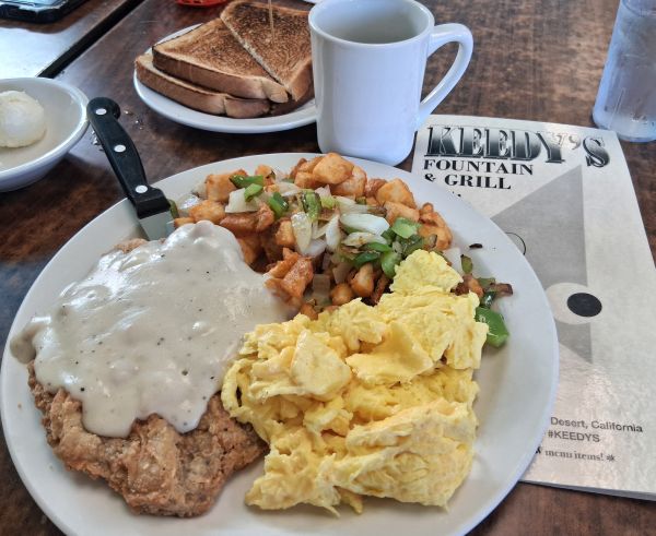 Plate of country fried steak with white gravy, scrambled eggs, home fries with peppers and onions, toast, coffee, and water at Keedy’s Fountain & Grill.