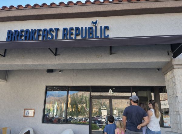 Exterior of Breakfast Republic in Palm Desert with a family standing near the entrance under the blue restaurant sign.