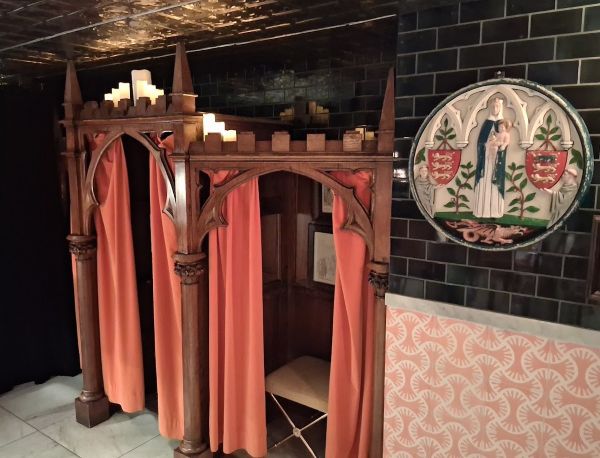 Decorative confessional booth at Counter Reformation with orange curtains, candles, carved wood, and religious iconography.