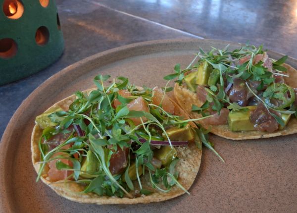 Two tuna tostadas topped with avocado, grapefruit, jalapeño, red onion, and microgreens on a ceramic plate.