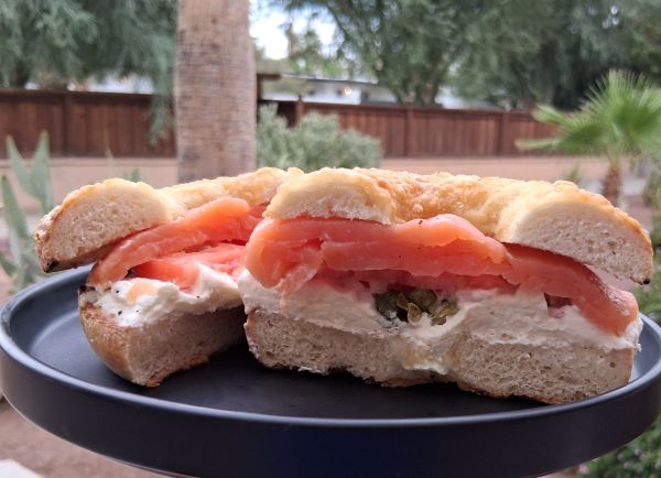 Close-up of a sliced lox and cream cheese bagel with capers on a dark plate in an outdoor Palm Springs setting.