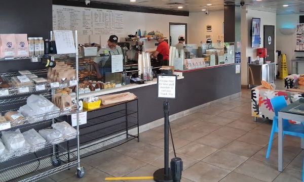 Townie Bagels interior counter with staff preparing drinks, pastry racks, and a large menu board overhead.
