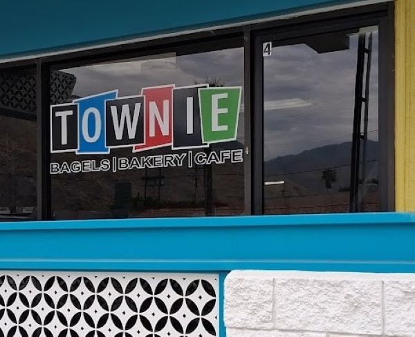 Colorful “TOWNIE Bagels | Bakery | Café” window sign framed by turquoise trim on Sunny Dunes in Palm Springs.