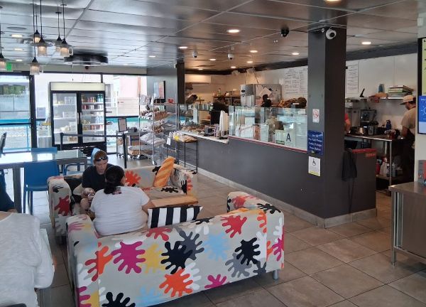 Colorful lounge seating inside Townie Bagels with customers talking near pastry cases and the service counter.