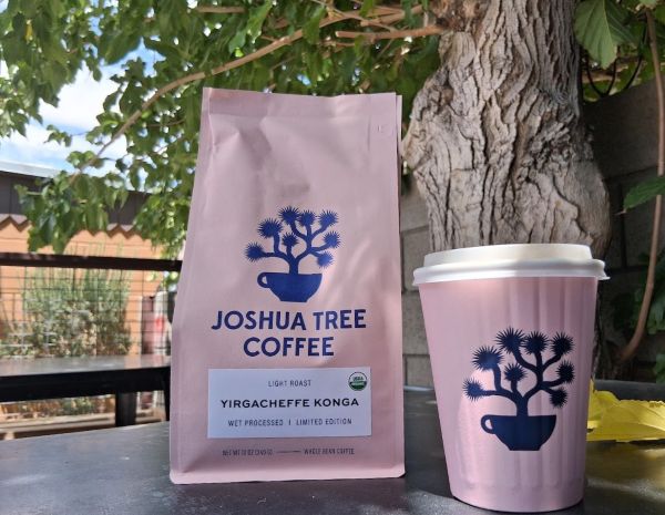 A logo'd coffee cup and coffee beans for Joshua Tree coffee set against a green background