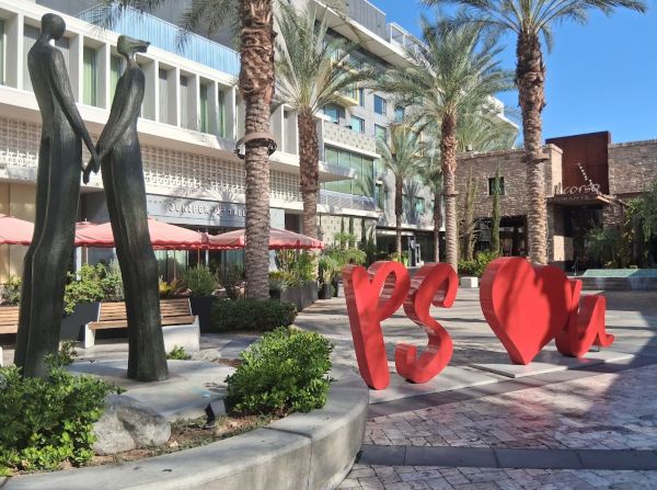 Palm Springs plaza featuring the PS ♥ U sculpture, palm trees, and surrounding restaurants.
