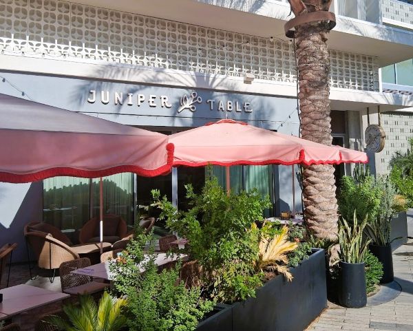 Outdoor patio at Juniper Table with pink umbrellas, modern façade, and lush planters.