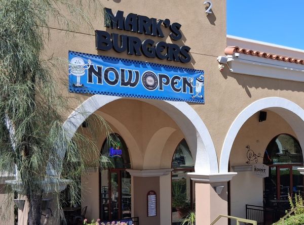 The exterior of Mark’s Burgers in Cathedral City, showing the tan building, arched windows, and a large “Now Open” sign.
