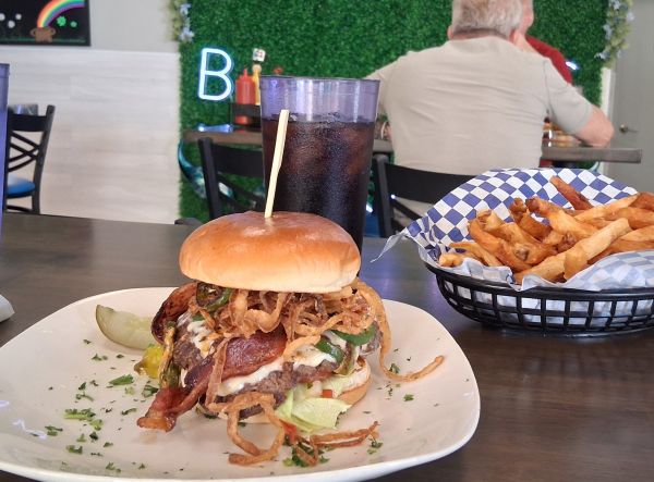A close‑up of the Juana Gallo smashburger at Mark’s Burgers, served with fries and a Diet Coke inside the restaurant’s dining area.