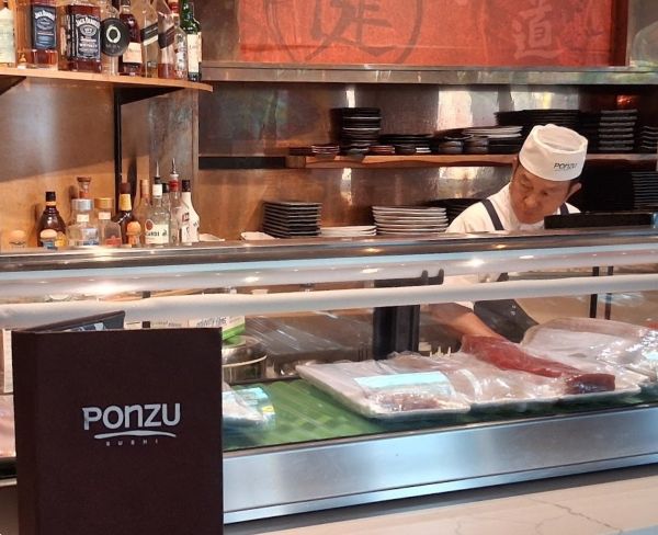 Chef preparing sushi behind the counter at Ponzu Sushi in downtown Palm Springs, with the restaurant’s menu in the foreground.