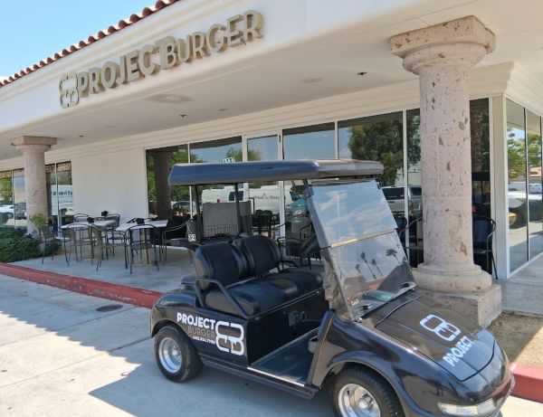 Exterior of Project Burger in Palm Desert with outdoor seating and a branded golf cart parked out front.