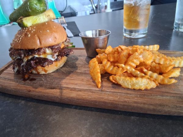 The Pika Pika burger topped with a pickle spear, melted cheese, and crispy smash patties, served with crinkle‑cut fries.