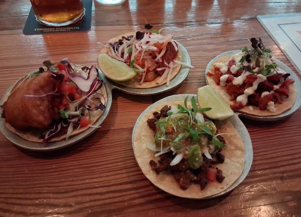 Four assorted tacos on individual plates with garnishes