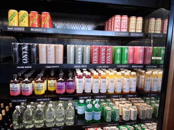 Beverage fridge at Bird Palm Springs stocked with wine coolers, non‑alcoholic cocktails, Onyx coffee drinks, kombucha, and Little West juices.