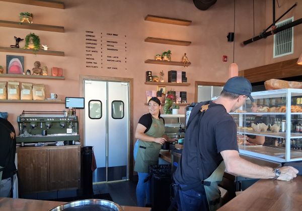 Baristas preparing drinks behind the counter at Bird Palm Springs with the coffee and cold brew menu displayed above the double doors.