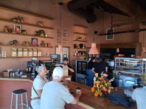 Interior of Bird Palm Springs featuring terracotta shelves, plants, coffee bags, and guests seated at the counter while baristas prepare drinks.