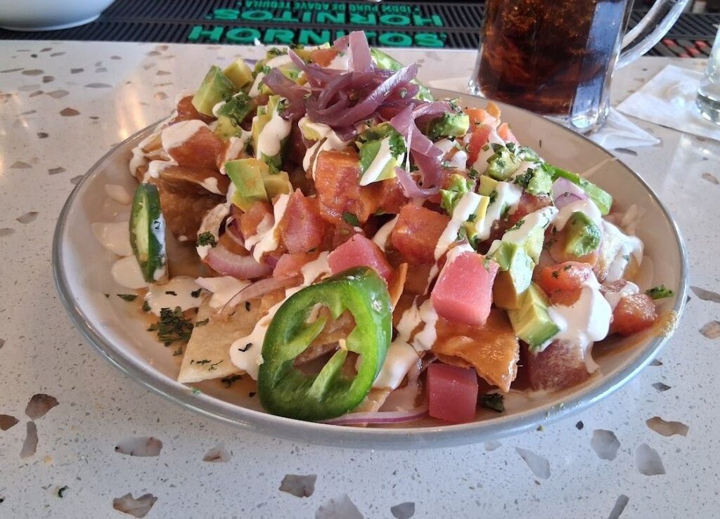 Nachos topped with raw tuna, avocado, jalapeños, red onion, herbs, and crema