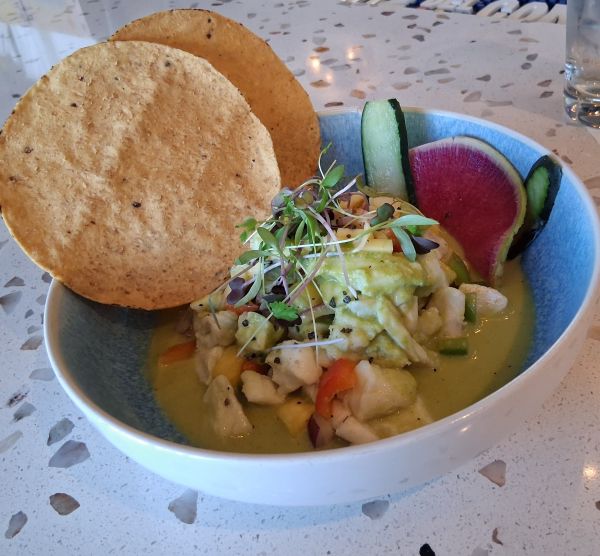 Bowl of ceviche topped with microgreens, served with tostadas, cucumber slices, and watermelon radish
