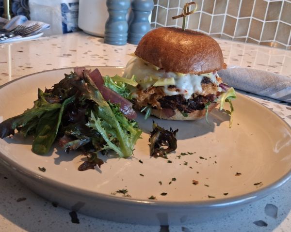 Crabcake sandwich on a brioche bun with melted cheese and a side salad