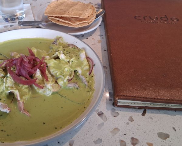Shrimp Aguachile in green sauce with red onions, tostadas, and the Crudo Cevichería menu beside the plate