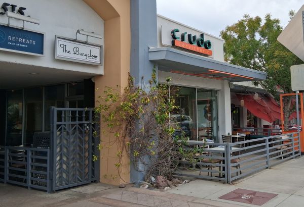 Street‑level view of Crudo Cevichería with patio seating and neighboring storefronts