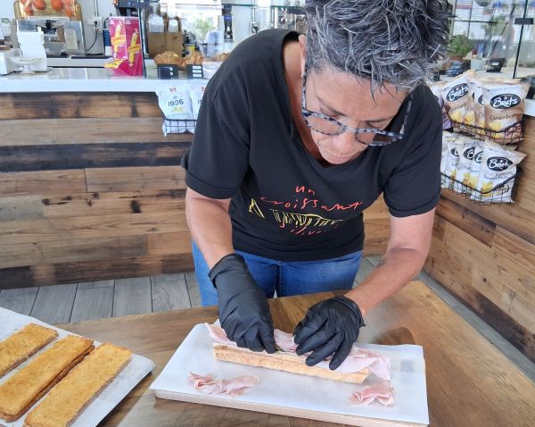 Candice preparing a sandwich behind the counter, layering ham onto fresh bread with precision.