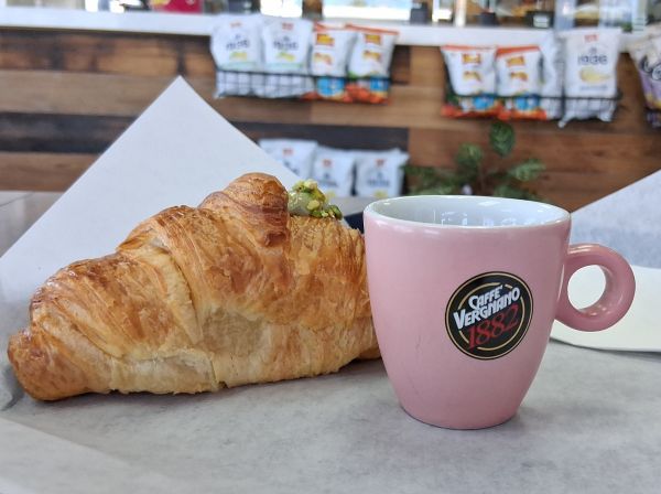 A pistachio croissant served beside a pink Caffè Vergnano espresso cup inside the café.
