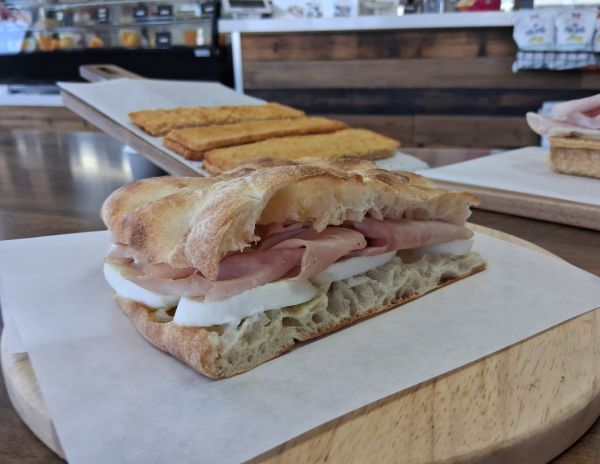 A rustic schiacciata sandwich filled with Italian meats and cheeses, presented on parchment inside the café.