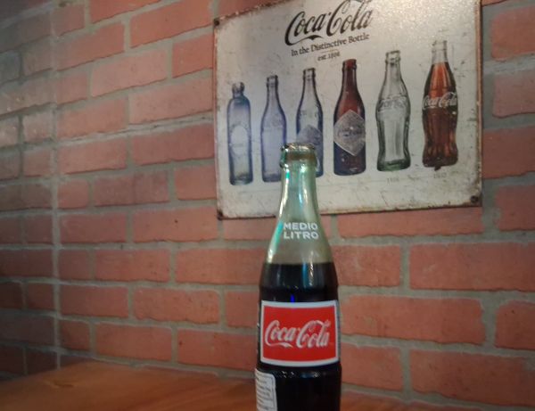 A made in Mexico Cocoa Cola bottle on El Tranvia's wooden table. Classy brickwork in the background and a vintage Cocoa Cola sign