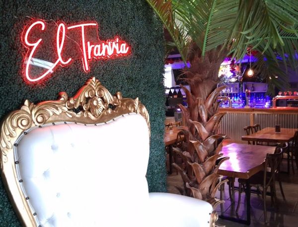 Tranvia sign above a white and gold throne chair, with the bar and a palm tree behind it