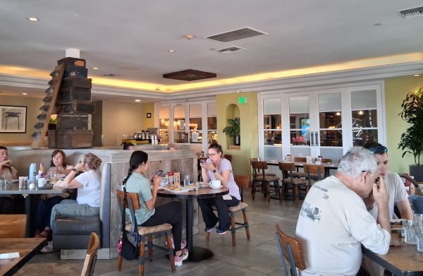Dining room at Wilma & Frieda in Palm Springs with round tables, banquette seating and a stacked crate display.