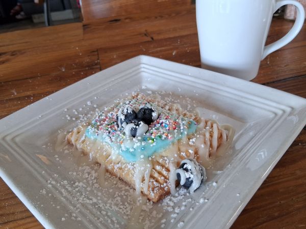 Pop Tart with blue icing, sprinkles, blueberries and powdered sugar on a white plate at Wilma & Frieda in Palm Springs.